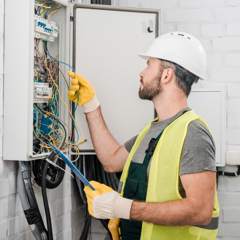 side view of electrician holding clipboard and checking wires in electrical box in corridor